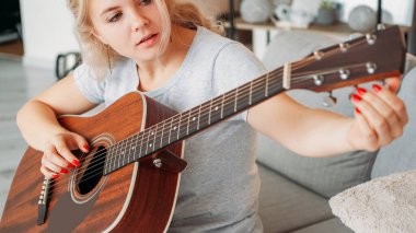 Akort aleti. İlham verici bir kadın. En sevdiğim hobi. Kadın oyuncu, akustik gitar sesini ayarlıyor. Oturma odasının iç tarafındaki koltukta..