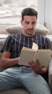 Dikey video. Okumaktan zevk alıyorum. Hafta sonu tatili. Rahatlatıcı hobi. Huzurlu bir adam, evinde gündüzleri en çok satanlar kitabıyla rahat bir koltukta oturuyor..