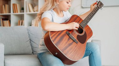 Gitarist. İlham verici bir kadın. En sevdiğim hobi. Düşünceli bir bayan, müzik aletinin tellerini ayarlıyor. Işıklı odada koltukta oturuyor..