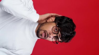 Dikey video. Dedikodu şoku. Gizli sürpriz. Kırmızı fotokopi arkaplanından izole edilmiş garip, sersemlemiş bir adam kulak misafiri..