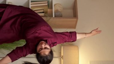 Dikey video. Ev içi yoga. Aktif yaşam tarzı. Bedensel zihin sağlığı. Neşeli kadın oturma odasında esneklik egzersizi yapıyor..