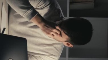 Dikey video. Fazla mesai. Son teslim tarihi stresi. İş yorgunluğu. Uykucu, yorgun, serbest çalışan, dizüstü bilgisayarda yazan, işini bitiren, gözlerini ovuşturan, karanlık ofis odasında uyuyan bir erkek..