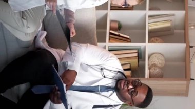 Dikey video. Sağlık hizmetleri meslektaşları. Doktorlar konuşuyor. Klinik teşhisi. Erkek doktor ve kadın hemşire hastane kanepesinde röntgen ve tıbbi geçmişi hakkında konuşuyorlar..