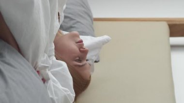 Dikey video. İyi sabahlar. Uyum motivasyonu. Yeni bir gün. Pozitif ilham kaynağı kaygısız kız uyandığında yatak odasındaki perdeyi açan enerjiyi hisseder..
