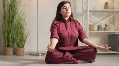 Meditasyon pratiği. Yoga içeride. İç huzuru. Nilüfer çiçeğinde oturan rahat, düşünceli kadın, evinde boş bir alanda, Gyan Mudra hareketi yapıyor..