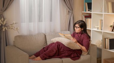 Boş zamanlarımda kitap okurum. Okuma akşamı. Hafta sonu evde. Huzurlu genç bir kadın ilginç bir hikayenin tadını çıkarıyor. Oturma odasındaki kanepede dinleniyor..