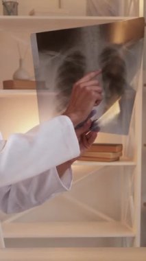 Dikey video. Teşhis konsültasyonu. Çevrimiçi doktor. Akciğer hastalığının röntgenini açıklayan zeki bir tıp uzmanı hastanenin iç kısımlarında oturuyor..