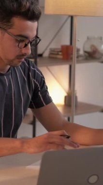 Dikey video. Mesafe. İş belgeleri. Odaklanmış iş adamı kağıt rapor verileri üzerinde çalışıyor. Bilgisayarda kayıt tutuyor. Ev ofisinin masasında oturuyor..