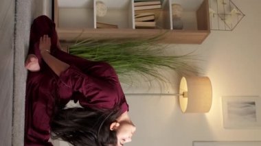 Dikey video. Yoga esneme hareketleri. Esneklik egzersizi. Aktif hobi. Dikkatli kadın bacak egzersizi yapıyor. İdman güvercini pozu veriyor. Oturma odasında eğiliyor..
