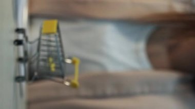 Dikey video. Çevrimiçi sipariş. İnternet mağazası. Dizüstü bilgisayarı iten, parmağını hareket ettiren, paketin teslim edilmesini bekleyen düşünceli genç kadın..