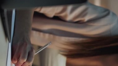 Dikey video. El yazısı. Çevrimiçi çalışma. Tanımlanamayan bir kadın kalemle sınav sınavına hazırlanıyor ve laptopla üniversite için rapor hazırlıyor..