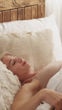 Dikey video. Kötü bir uyku. Rahatsız edici bir yatak. Evdeki boş alanda battaniyeyle örtülü yatak ve yastıkların üzerinde dönüp duran canı sıkkın bir kadın..
