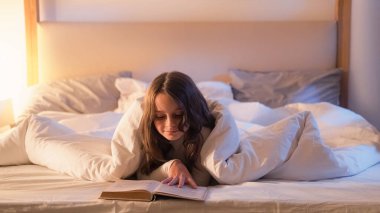 Çocuk eğlencesi. Gece barışı. Sanat fantezisi. Rahat, meraklı küçük kız uyumadan önce kitap okuyor. Yatak odasında sıcak lambayla yatıyor..