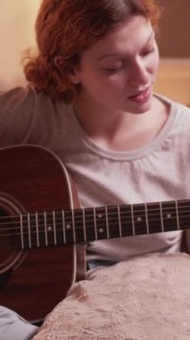 Dikey video. Gitar dersi. Çevrimiçi müzik dersi. Gülümseyen kadın müzisyen akustik enstrüman çalıyor evde dizüstü bilgisayar dersinde akorları gösteriyor.