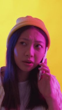 Dikey video. Telefon sorunu. Mobil iletişim. Ciddi bir kadın, el ele tutuşup konuşuyor. Bağlantı kötü. Pembe ışıklar sarı arka plan..