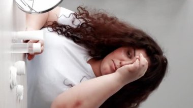 Dikey video. Göz bakımı altında. Deri rutini. Kozmetik ürünü. Yaşlanma karşıtı tedavi. Kilolu obez kadın temiz yüzüne nemlendirici krem sürüyor..