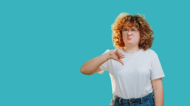 Nefret dolu bir jest. Olumsuz geri besleme. Mide bulandırıcı, gözlüklü tombul kız mavi fotokopi arkaplanında izole bir şekilde baş parmağını gösteriyor..