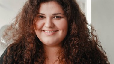 Tombul, güzel, gülen surat. Sağlıklı yaşam. Vücut pozitif. Neşeli, mutlu, kilolu, açık tenli, siyah kıvırcık saçlı bir kadının portresi..