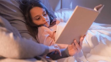 Gece masalı. Yatmadan önce kitap oku. Çocuk uykusuzluğu. Ebeveyn yaşam tarzı. Anne kitaptaki resimlerini, yatak odasında yatan yorgun küçük kıza gösteriyor..