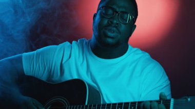 Vokalist gösterisi. Akustik festivali. Yetenekli müzisyen gitarist telli enstrüman çalıyor. Parlak neon ışığı altında duman içinde şarkı söylüyor..