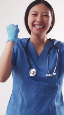 Dikey video. Heyecanlı doktor. Kazanan jest. Neşeli, mutlu hemşire kadın mavi üniforma giyiyor. Kollarını kaldırıyor. Gülümsüyor..