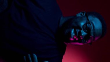 Dikey video. Onaylama jesti. İyi seçim. Güzel teklif. Neşeli, gülümseyen reklamcı adam başparmağını kaldırdı. Renkli kırmızı ışıklı arka plandaki işaret gibi..