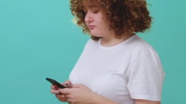 Mobil sohbet. Sosyal medya. Çevrimiçi iletişim. Tombul kız mavi boş arkaplanda izole edilmiş telefon kullanarak mesaj gönderiyor.