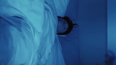 Dikey video. Kötü bir rüya. Gece dehşeti. Uyku korkusu. Korkmuş bir adam, karanlık yatak odasındaki şeytani el gölgesi kâbusundan uyandı..