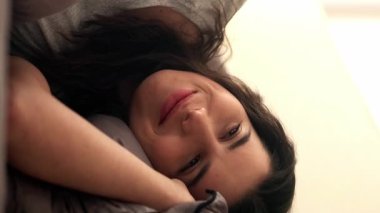 Dikey video. Huzur içinde yat. Sıcak yatak odası. Uyku zevki. Yumuşak, temiz çarşafların içinde, yorganın altında huzurlu, mutlu bir kadın..