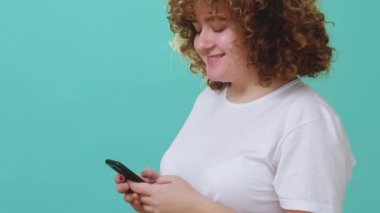 Çevrimiçi sohbet. Selfie mesajı. Dijital iletişim. Mutlu gülümseyen kıvrımlı kız mavi boş arkaplanda izole bir resim göndermek için telefon mesajı kullanıyor..