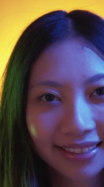 Dikey video. Mutlu görünüş. Neon portresi. Pozitif, narin, neşe saçan kadın, yakından gülümse. Yüzün canlı, güzel, taze, yeşil, açık mavi neon..