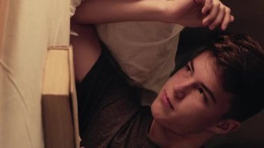 Dikey video. Gece kitabı. Yorgun genç bir adam huzurlu bir ortamda uykuya dalıyor. Derin düşüncelere dalmış huzurlu bir ışıkla banyo yapıyor..
