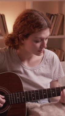 Dikey video. Müzik alıştırması. Gitar keyfi. Evde oturma odasındaki kanepede akustik bir enstrüman çalan müzisyen kızdan esinlendim..