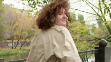 Mutlu bir gün. Aktif yaşam tarzı. Özgürlük sevinci. Kıvırcık saçlı neşeli, güler yüzlü kız sonbahar parkında koşmaktan zevk alıyor..