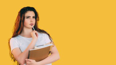 Düşünceli öğrenci. Akıllıca bir düşünce. Not defteri olan kafası karışık bir kız, sarı boş alan arka planında izole edilmiş fikirleri düşünüyor..