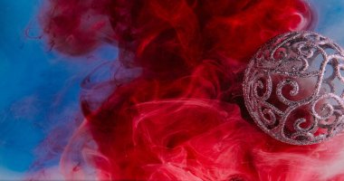 Parlak süs. Boya suyu sıçraması. Duman bulutu soyut arka planında odaklanmış, parlak, mavi, kırmızı, değerli bir Noel süslemesi..