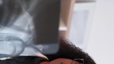 Dikey video. Doktor uzmanlığı. Radyoloji uzmanı. Hastane sağlık hizmetleri. Klinikte teşhis tedavisi için röntgeni inceleyen odaklanmış zeki kadın doktor..