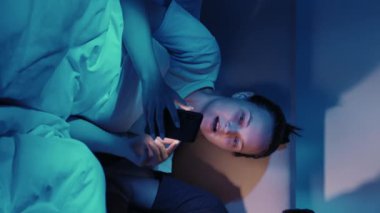 Dikey video. Genç çift gece lambasıyla aydınlatılan akıllı telefon dizüstü bilgisayarında sohbet ediyor..
