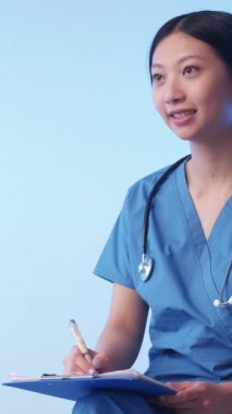 Dikey video. Tıbbi danışmanlık. Sağlık hizmetleri. Mutlu kadın doktor üniforması oturan konuşan hasta tanıyı yazıyor mavi arka plan boş alan.