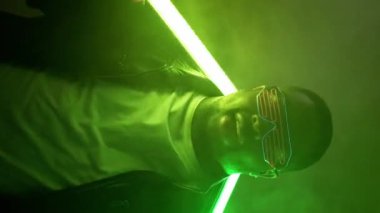 Dikey video. Rap şovu. Gece kulübü performansı. Havalı, kendine güvenen, modaya uygun güneş gözlüklü neşeli bir adam hip hop etkinlik sahnesinde parlak neon lambalı arka planda şarkı söylüyor..