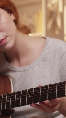 Dikey video. Müzik hobisi. Gitar akordu. Akustik yetenek. Konsantre kadın müzisyen evdeki mandal ve vites ayarlıyor..