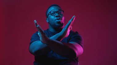 Jest yok. Reddetmek. Yüzünde hoşnutsuzluk ifadesi olan, elleri çaprazlanmış, kırmızı arka planda izole edilmiş neon ışıkta reddedilmiş ciddi bir adam..