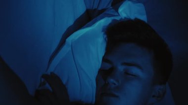 Vertical video. Night terror. Bad dream. Anxiety stress. Disturbed scared guy woke up opened eyes in bed late at home in dark blue light.