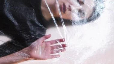 Dikey video. Plastik ambalaja bastıran kadın yalnızlığı sembolize ediyor. Duygusal engeller, yalnızlık..