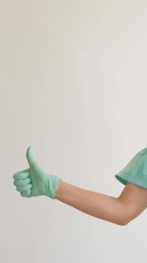 Dikey video. Virüs korunuyor. Kapalı güvenlik. Tıbbi maske takan kız güneş gözlüğü takıyor. Baş parmağıyla destekliyor. Salgın tarzında, beyaz arka planda izole edilmiş..