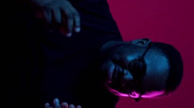 Dikey video. Kazanan dans. Zafer kutlaması. Aşırı neşeli, heyecanlı, gülümseyen adam, koyu kırmızı arka planda izole edilmiş neon ışıkla tatmin olmuş..