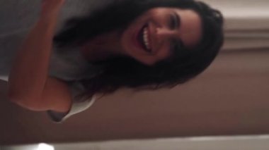 Dikey video. Milenyum yaşam tarzı. Kaygısız kadın. Hafta sonu eğlencesi. Mutlu kadın yatakta dans ediyor, rahat yatak odasında..