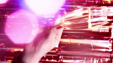 Dikey video. Kutlama içkisi. Xmas partisi. Parlak kırmızı bir arka planda, renkli bir bokeh ışığıyla köpüklü şarap kadehini tutan bir kadın..