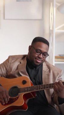Dikey video. Gitar ilhamı. Şarkı çalıyor. Neşeli yetenekli müzisyen, evde evdeki kanepede akustik telli enstrüman ile caz akorlarını dinliyordu..