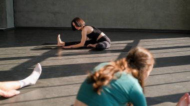 Jimnastik eğitimi. Germe egzersizi. Formda kadın yoga eğitmeni grup esneme egzersizleri öğretiyor spor salonundaki spor salonundaki paspasın üzerinde egzersiz yapıyor..